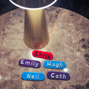 Custom 3D-printed name badges on a marble table, labelled Chris, Emily, Hugh, Neil, and Cath.